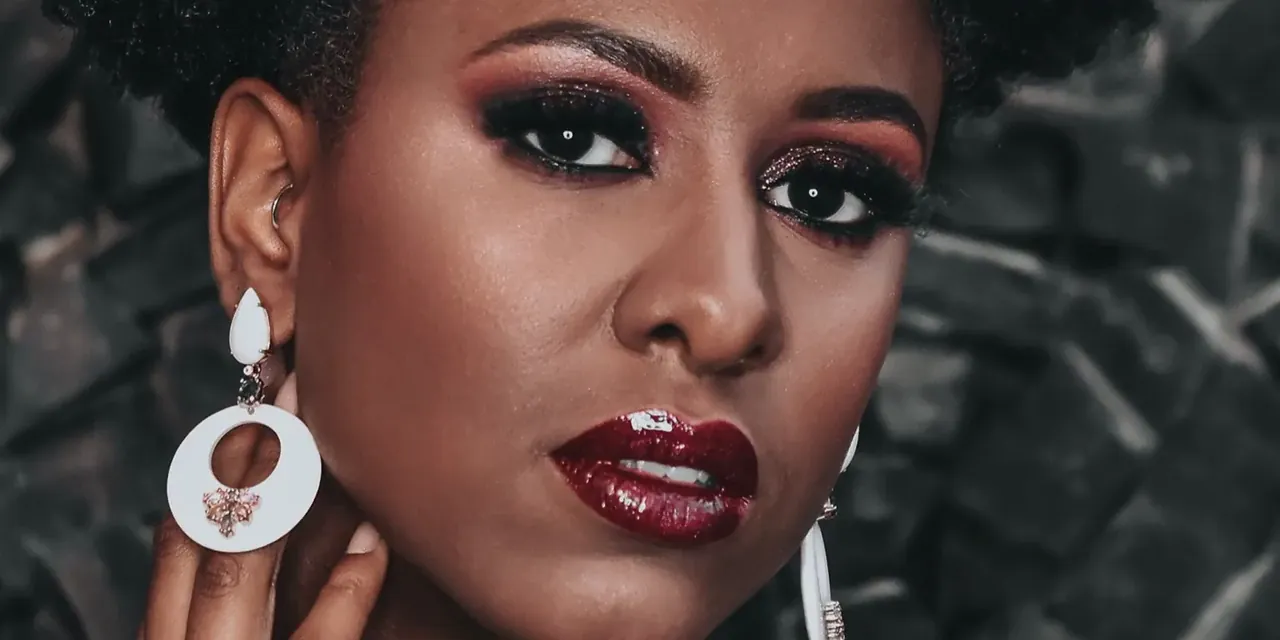 A client's face in close-up, dark eye make-up and deep red lip, against dark stone